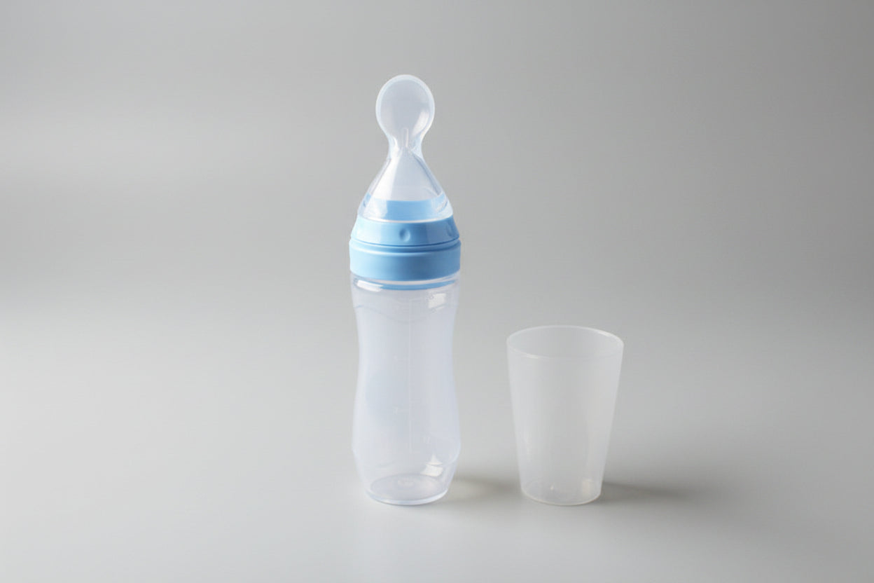 Baby bottle with blue cap and clear cup on a beige surface with green plant in the background