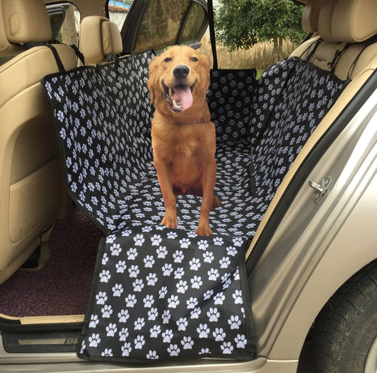 Dog sitting on a black and white paw print car seat cover in a vehicle.